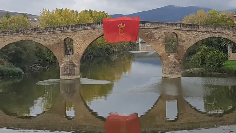 Una gran bandera de Navarra enarbolada en el emblemático puente de Puente la Reina CEDIDA