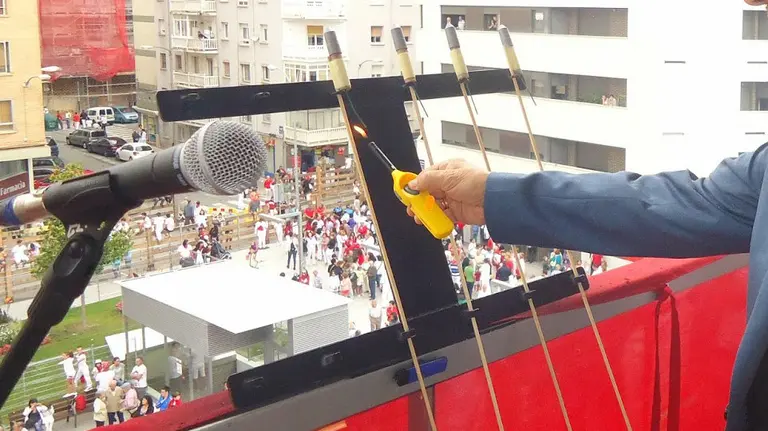 Una persona enciende un cohete festivo desde un balcón consistorial