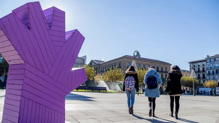 Varias personas pasean junto a una de las grandes manos que simbolizan en la Plaza del Castillo el rechazo a las agresiones sexistas. ALZUGARAY