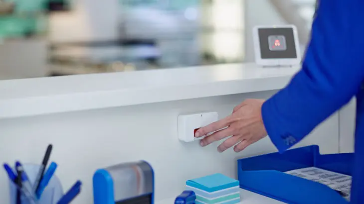 Una funcionaria aprieta el botón del pánico empleado en caso de intentos de agresión a personas que trabajan de cara al público VERISURE