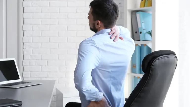 Un hombre se lleva las manos a la espalda mientras trabaja frente a un ordenador en una oficina ARCHIVO