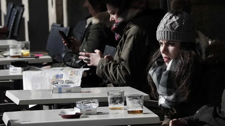 Una joven bien abrigada toma en una terraza de la Plaza del Castillo de Pamplona en un día con tiempo muy frío aunque sin nieve en la capital navarra. EFE/ Jesús Diges