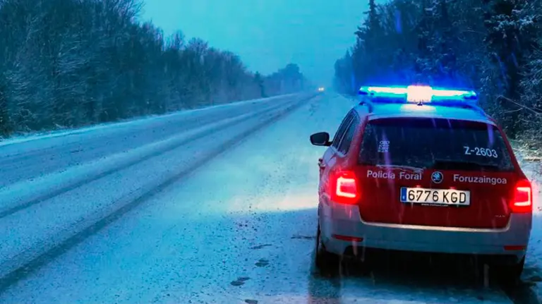 Un coche de la Policía foral vigila una carretera de Navarra cubierta de neive