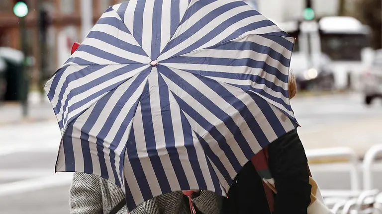 Dos mujeres se protegen con un paragüas de la lluvia y el viento en Pamplona, en una jornada en la que el Ayuntamiento de la capital navarra ha activado la alerta por vientos fuertes a partir de esta tarde y ha desactivado el Plan de Nieve que puso en marcha el pasado martes. EFE/Jesús Diges