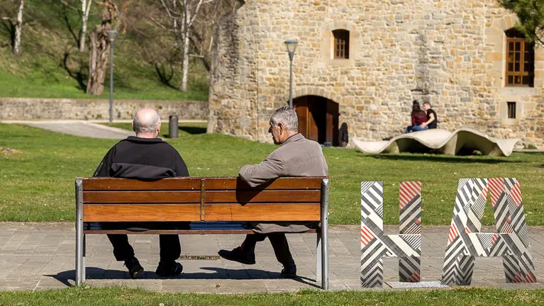 Varias personas charlan en la Ciudadela junto al nuevo logotipo de Hiriartea.