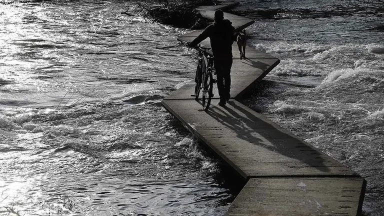 GRAF2186. PAMPLONA, 28/03/2018.- Una persona atraviesa las pasarelas del río Arga que debido a las altas temperaturas y al deshielo de la nieve en las montañas bajaba con una fuerte corriente. EFE/Jesús Diges