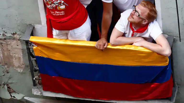 Varias personas se congregan en un balcón de una calle de Pamplona para ver uno de los encierros de San Fermín
