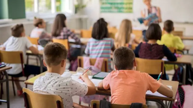 Unos niños atienden en sus pupitres las explicaciones de su profesora durante una clase en el colegio ARCHIVO