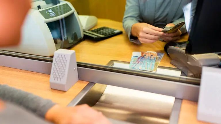 Imagen de archivo de una empleada de banco contando billetes para entregárselos a un cliente que espera al otro lado de la ventanilla ARCHIVO