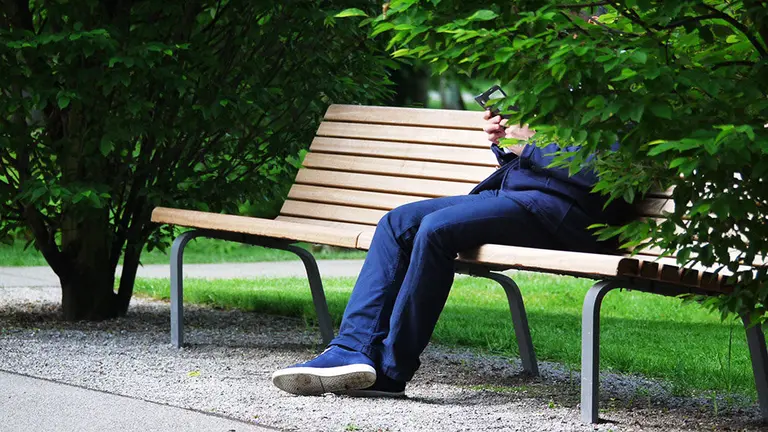 Imagen de un hombre mandando mensajes a través de su teléfono móvil en un parque ARCHIVO