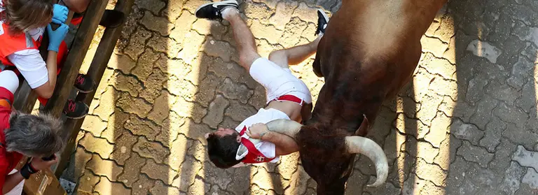 Un mozo es enganchado y golpeado por un toro de Miura por la camiseta y el pañuelo en el callejón durante el octavo encierro de San Fermín 2018. REUTERS/Susana Vera