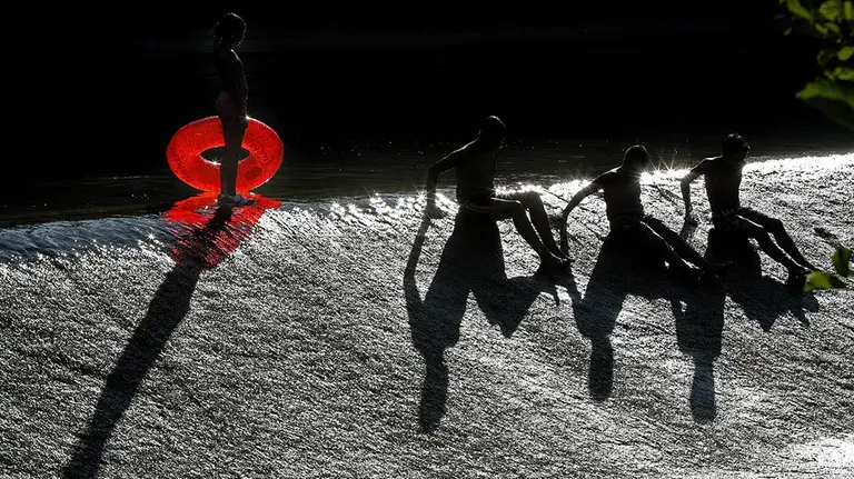 Varios jóvenes con unos flotadores se divierten en el río Arga a su paso por Pamplona en un día marcado por el tiempo soleado y el calor veraniego. EFE/Villar López
