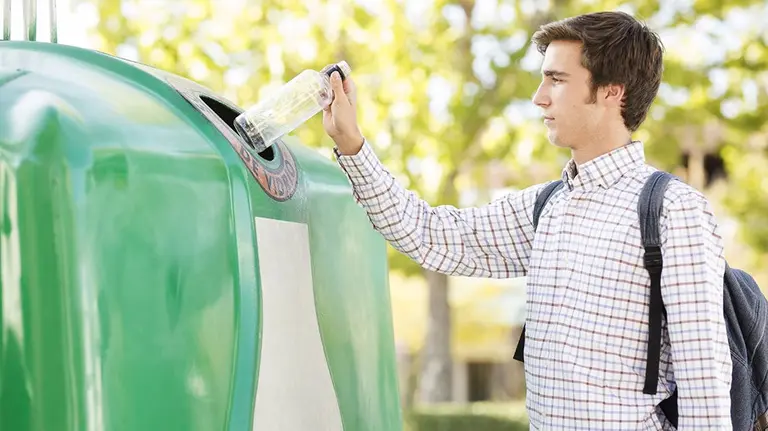 Un joven deposita una botella en un contenedor para vidriO ECOVIDRIO