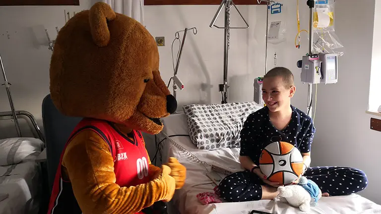 Alexandra Oliver con la mascota del equipo Ronky en la visita del Basket Navarra a los niños ingresados en el Complejo Hospitalario de Navarra. GOBIERNO DE NAVARRA