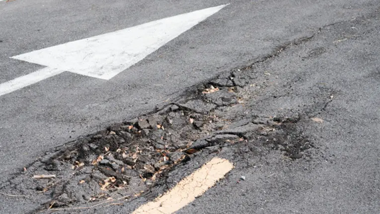 Imagen de una calzada con el asfalto levantado y un socavón en la grava ARCHIVO
