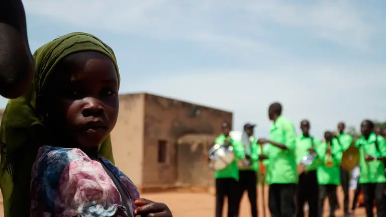 Una niña mira a la cámara mientras una banda toca música en Uganda. ARITZ AZPARREN