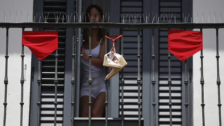 Una chica cierra la puerta de un balcón en una calle de Pamplona durante las fiestas de San Fermín. Archivo / EFE