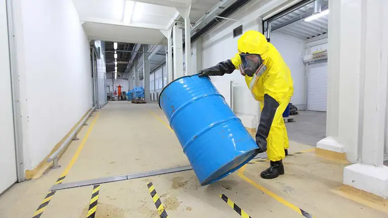 Un trabajador, cubierto con un buzo y una mascarilla para prevenir elementos tóxicos, carga un bidón con material peligroso ARCHIVO
