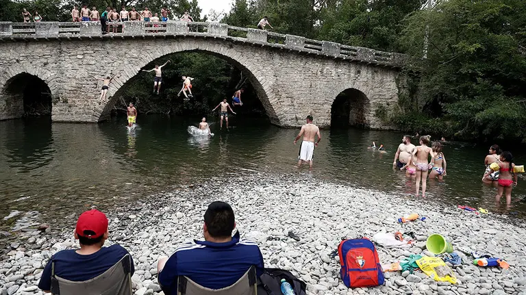 Dos personas observan sentados como varios jóvenes se tiran desde el puente de la localidad navarra de Irozt a las aguas del rio Arga en una jornada donde ha sido intenso el calor vivido este jueves en la comunidad foral donde las temperaturas han alcanzado los 40 grados. Según la Agencia de Meteorología, se recrudece la ola de calor en doce comunidades, nueve de ellas en naranja (riesgo importante) debido a la llegada a la península de una masa de aire africano muy cálida, muy seca y con polvo en suspensión. EFE/ Jesús Diges