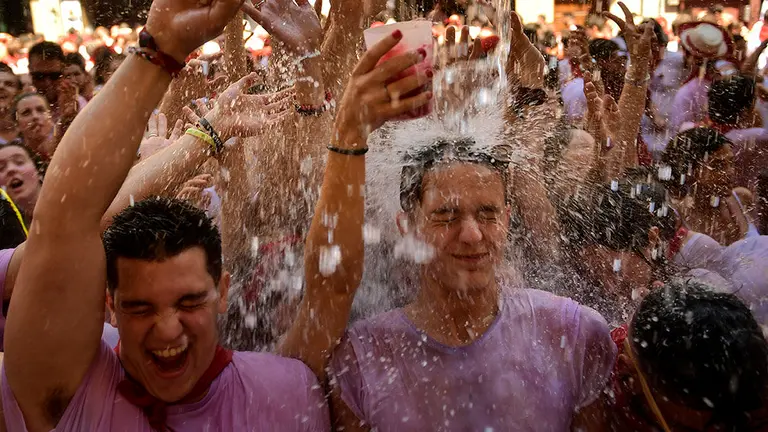 Varios jóvenes aguardan la llegada del agua desde los balcones de Pamplona tras el tradicional Chupinazo. AFP / REUTERS