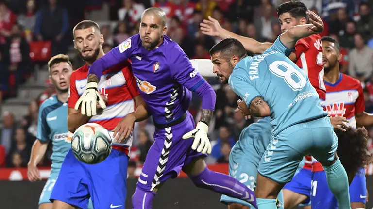 El guardameta de Osasuna, Rubén Iván Martínez (3i), intenta despejar el balón ante su compañero, Fran Mérida (d), y el defensa portugués del Granada, Domingos Duarte, durante el encuentro correspondiente a la novena jornada de primera división disputado esta noche en el estadio Nuevo Los Cármenes de Granada. EFE / Miguel Ángel Molina.