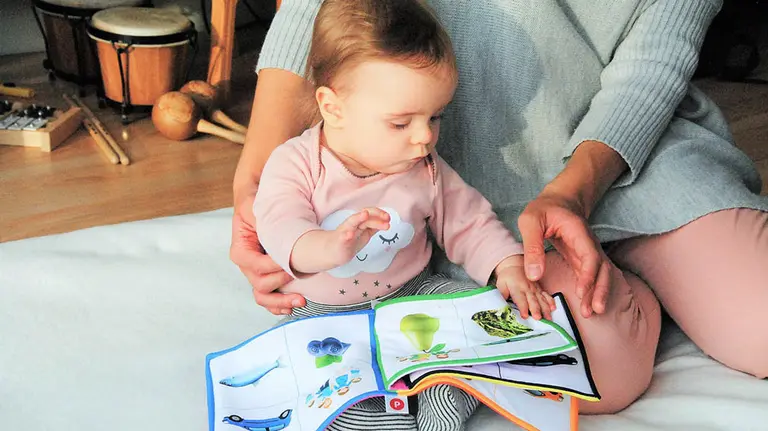Una madre acompaña a su bebé mientras observan un libro.