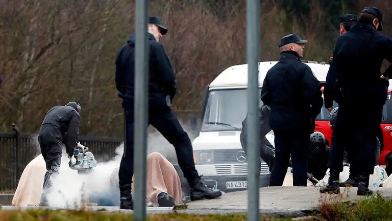 A national police agent cuts a concrete block to which various protesters have chained to in order to block a road in Pamplona, Navarra, Spain, during the general striked called 30 January 2020.  Unions called for a general strike in Basque Country and Navarra to demand steady jobs and minimum pensions of 1080 euros. EFE/ Jesus Diges
