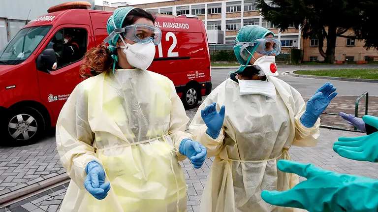 Dos enfermeras que acaban de trasladar en ambulancia a un enfermo que ha dado positivo en el test del COVID-19 solicitan ayuda de un efectivo de la DYA Navarra que en coordinación con el departamento de Salud ha implantado un túnel de desinfección en el Complejo Hospitalario de Navarra para desinfectar tanto ambulancias, como material médico intrahospitalario. El proceso de desinfección de las ambulancias se realiza con un tratamiento de ozono, agua y lejía, garantizando así que vuelva a salir limpia. EFE/ Jesús Diges