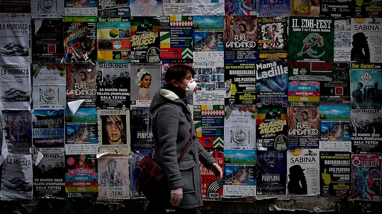 GRAF2358. PAMPLONA, 18/04/2020.- Una persona con mascarilla pasa este sábado en Pamplona por delante de decenas de anuncios de eventos culturales, todos ellos cancelados, durante el primer día de la sexta semana de confinamiento en casa declarado por la crisis sanitaria del coronavirus con el objetivo de prevenir la propagación del mismo. EFE/Villar López
