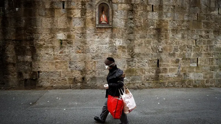 GRAFCAV4760. PAMPLONA, 21/04/2020.- Una mujer pasa por delante de la hornacina de San Fermín en la cuesta de Santo Domingo de Pamplona, primer tramo del encierro de los Sanfermines, en una jornada en la que el Ayuntamiento de Pamplona ha anunciado la suspensión de las fiestas de 2020 por la crisis del coronavirus. EFE/Villar López.