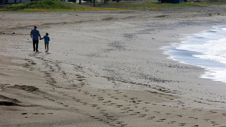 Un padre con su hijo paseando en una playa. Europa Press.