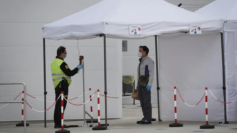 GRAFCAV4967. PAMPLONA, 27/04/2020.- Unos 1.600 empleados de la planta navarra de Volkswagen han retomado este lunes "con una mezcla de incertidumbre y satisfacción" la producción de vehículos, paralizada desde el pasado 15 de marzo por la pandemia del coronavirus. En la imagen momento en el que se le toma la temperatura a uno de los trabajadores antes de entrar a la factoría alemana en Navarra. EFE/ Villar López