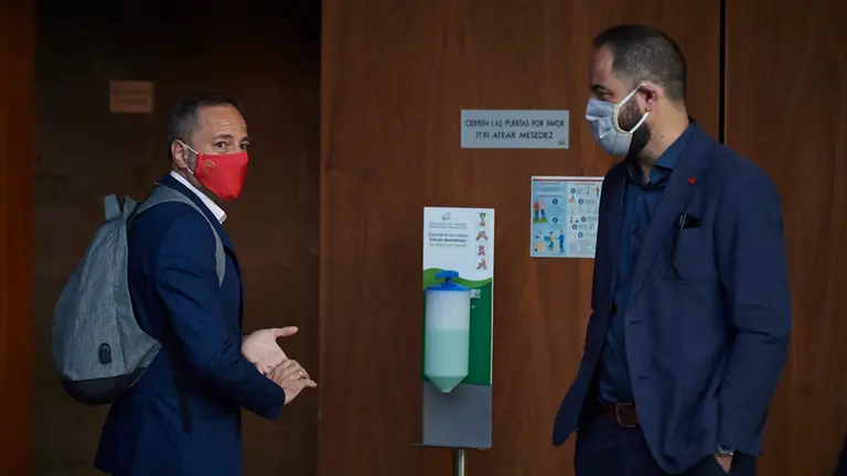 Juan Luis Sánchez de Muniain, se desinfecta las manos con gel mientras habla con el socialista Ramón Alzorriz. PABLO LASAOSA