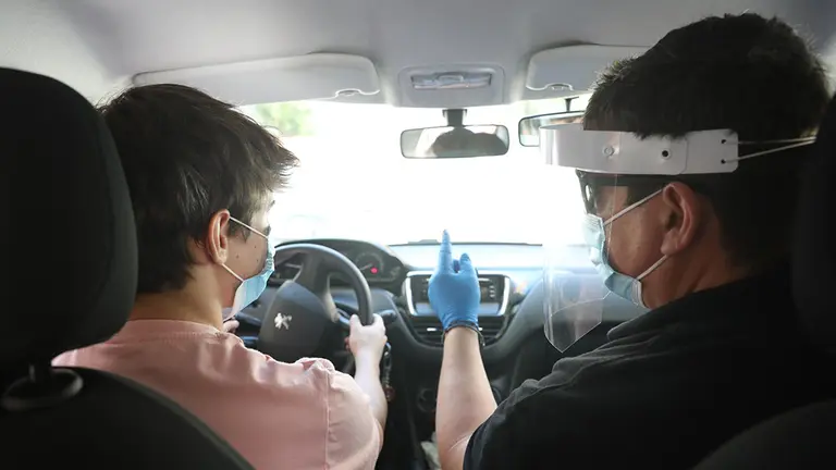 Un profesor de autoescuela, protegido con mascarilla, guantes y pantalla protectora, en una clase con un alumno. EUROPA PRESS