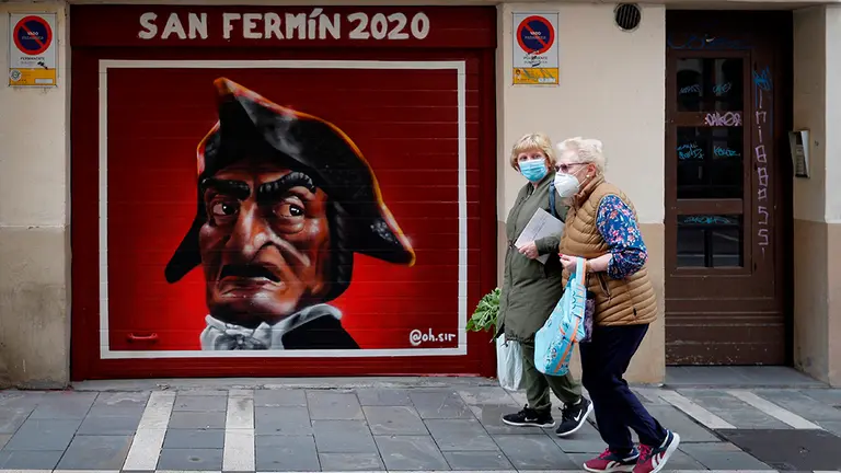 GRAFCAV6418. PAMPLONA, 09/06/2020.- Dos mujeres pasan por delante de un grafiti sobre los Sanfermines 2020 en una jornada en la que el Ayuntamiento de Pamplona se ha mostrado contrario a incentivar actividades que supongan aglomeraciones durante las fechas de las suspendidas fiestas de San Fermín 2020y rechaza también las aglomeraciones producidas este fin de semana en la capital navarra. EFE/ Villar López