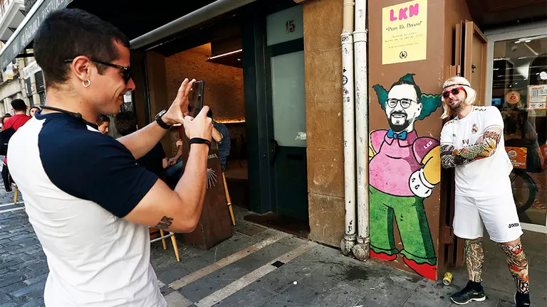 Una persona con la camiseta del Real Madrid se toma una fotografía junto a una caricatura del entrenador del Getafe, Pepe Bordalás, que ha sido motivo de noticia después de que el artista gráfico &#39;LKN&#39; haya plasmado el rostro del técnico del conjunto azulón sobre el cuerpo del famoso personaje de los Simpson &#39;Krusty el payaso&#39;. El artista lo ha realizado con motivo del encuentro que disputarán mañana ambos equipos en El Sadar, se trata de una alusión crítica del artista al técnico alicantino, quien realizó en la previa del partido de la primera vuelta unas polémicas declaraciones contra los rojillos, algo que ha aprovechado el grafitero para `calentar&#39; un encuentro en el que Osasuna y Getafe se juegan sus aspiraciones. EFE/Jesús Diges