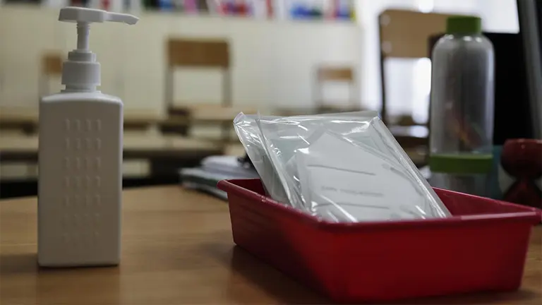 Mascarillas y gel desinfectante en la mesa del profesor de un aula. ARCHIVO