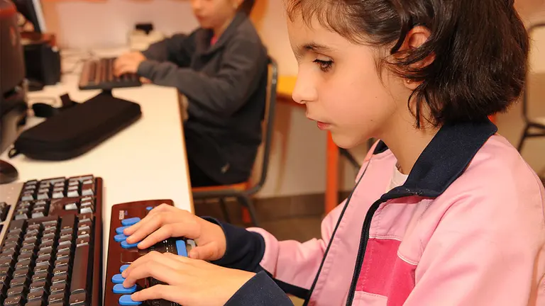 Alumnas de Educación Primaria utilizando ordenadores adaptados, uno de ellos con linea braille. ONCE