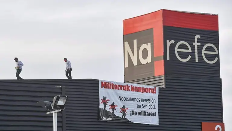 Dos personas acceden al tejado de Refena para colgar una pancarta pidiendo la marcha de los militares de Navarra. TWITTER