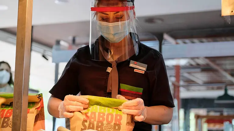 Una empleada protegida con pantalla, mascarilla y guantes prepara un pedido en un establecimiento de Burger King, dentro del plan Más Seguro que nunca que la cadena ha puesto en marcha en todos sus establecimientos abiertos con una serie de estrictas medidas de seguridad, que incluyen límite de aforo y mamparas de separación, además de donar más de 16.000 menús a sanitarios y cuerpos y fuerzas de seguridad, en Madrid (España), a 13 de mayo de 2020.
13 MAYO 2020 CORONAVIRUS;BURGER KING;COVID-19;
Jesús Hellín / Europa Press
  (Foto de ARCHIVO)
13/5/2020