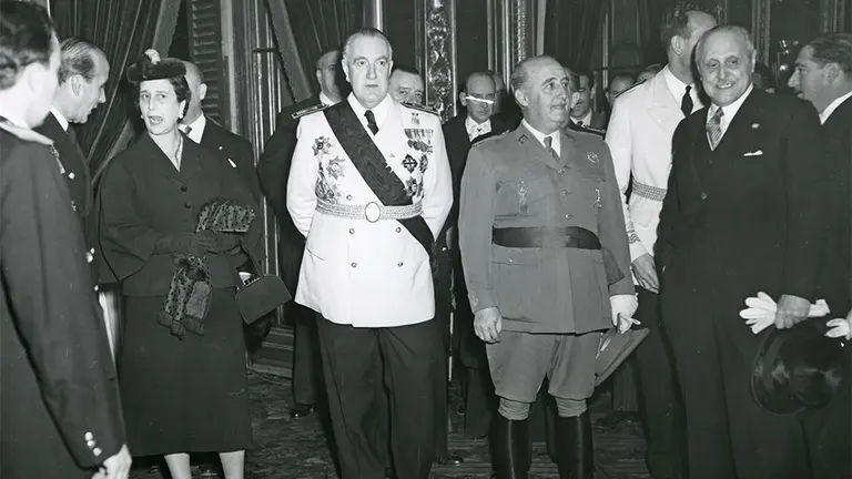 Vista parcial de la recepción de autoridades ofrecida en el Palacio de Navarra, en Pamplona, con motivo de la visita del jefe del Estado, general Franco. En el centro, Carmen Polo de Franco; Fernando Suárez de Tangil, conde de Vallellano, ministro de Obras Públicas; el general Francisco Franco. 2 de diciembre de 1952. portalcultura.navarra.