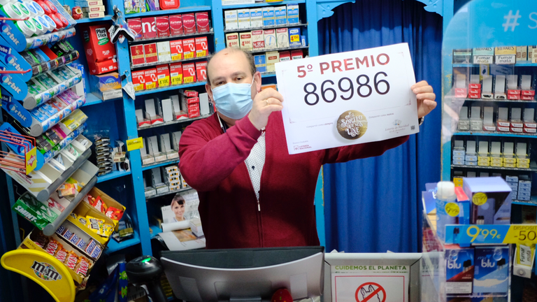 El propietario de la administración de lotería de la calle Ciudadela de Pamplona posa junto con el primer quinto premio de la lotería de Navidad 2020. PABLO LASAOSA(1)