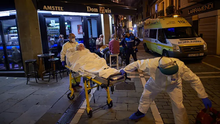 Una mujer con coronavirus es trasladada desde su domicilio por personal sanitario mientras la gente esta dentro de los bares durante la crisis de la pandemia. MIGUEL OSÉS