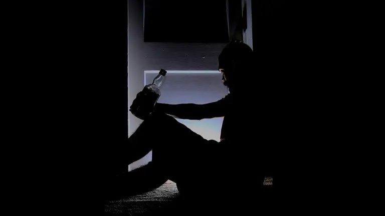 Un hombre borracho sentado en el suelo con una botella de alcohol ARCHIVO