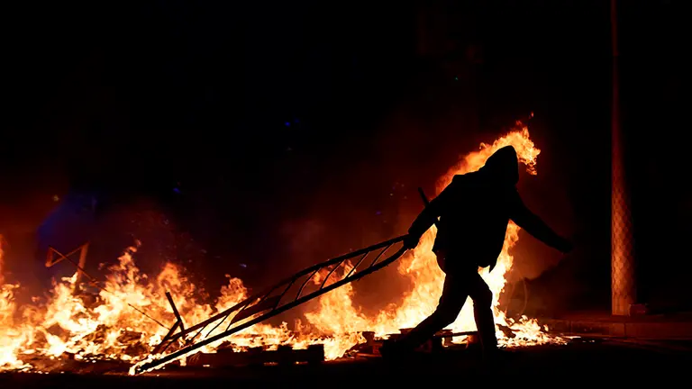 Un manifestante lanza una valla a la barricada en llamas en la calle Aragó en las protestas por el encarcelamiento del rapero Pablo Hasel, a quien este jueves le fue confirmada otra condena a prisión por amenazar a un testigo, esta noche en Barcelona. EFE/Alejandro García