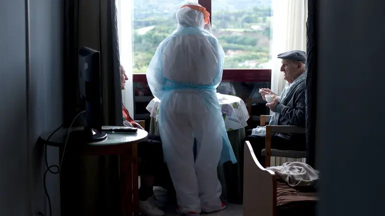 Una trabajadora de la residencia San Carlos de Celanova (Ourense) vestida con un EPI para protegerse del Covid sirve el desayuno a unos ancianos. EFE/Brais Lorenzo