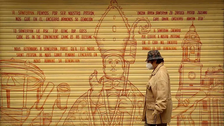 GRAFCAV4769. PAMPLONA, 21/04/2020.- Una mujer pasa por delante de un graffiti de San Fermín en la curva de Mercderes de Pamplona en una jornada en la que el Ayuntamiento de Pamplona ha anunciado la suspensión de las fiestas de 2020 por la crisis del coronavirus. EFE/Villar López