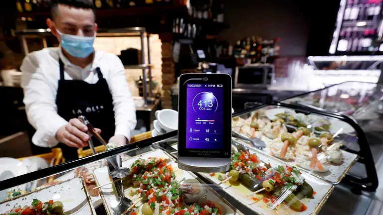 Un camarero sirve desde la barra de un bar de Pamplona un pincho donde se muestra un medidor de CO2 que mide la calidad del aire que en esos momentos presenta su interior con una buena calidad del mismo. EFE/ Jesús Diges