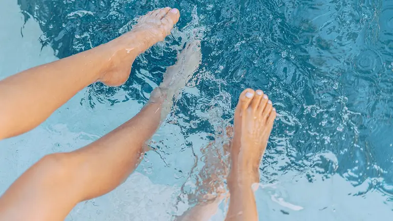 Dos personas con los pies metidos en la piscina. ARHCIVO
