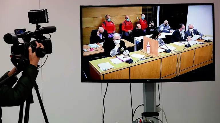 GRAFCAV5465. PAMPLONA, 24/05/2021.- Imagen tomada del televisor de la sala de la Audiencia Provincial de Navarra que acoge desde este lunes el juicio con jurado por un triple crimen perpetrado en Cáseda en septiembre de 2018, tras el enfrentamiento entre dos familias. En sus conclusiones provisionales, el fiscal solicita 60 años de prisión —20 por cada uno de los tres delitos de asesinato— para los tres acusados —padre y dos hijos— de la muerte de Fermín J.E., de 50 años, y de dos de sus hijos, José Antonio y Cristian, de 20 y 17 años, quienes fallecieron a consecuencia de los disparos de escopeta recibidos. En la imagen, el fiscal (i), el abogado de la acusación particular (detras), los abogados de los acusados y detrás los tres procesados.  EFE/ Jesús Diges
